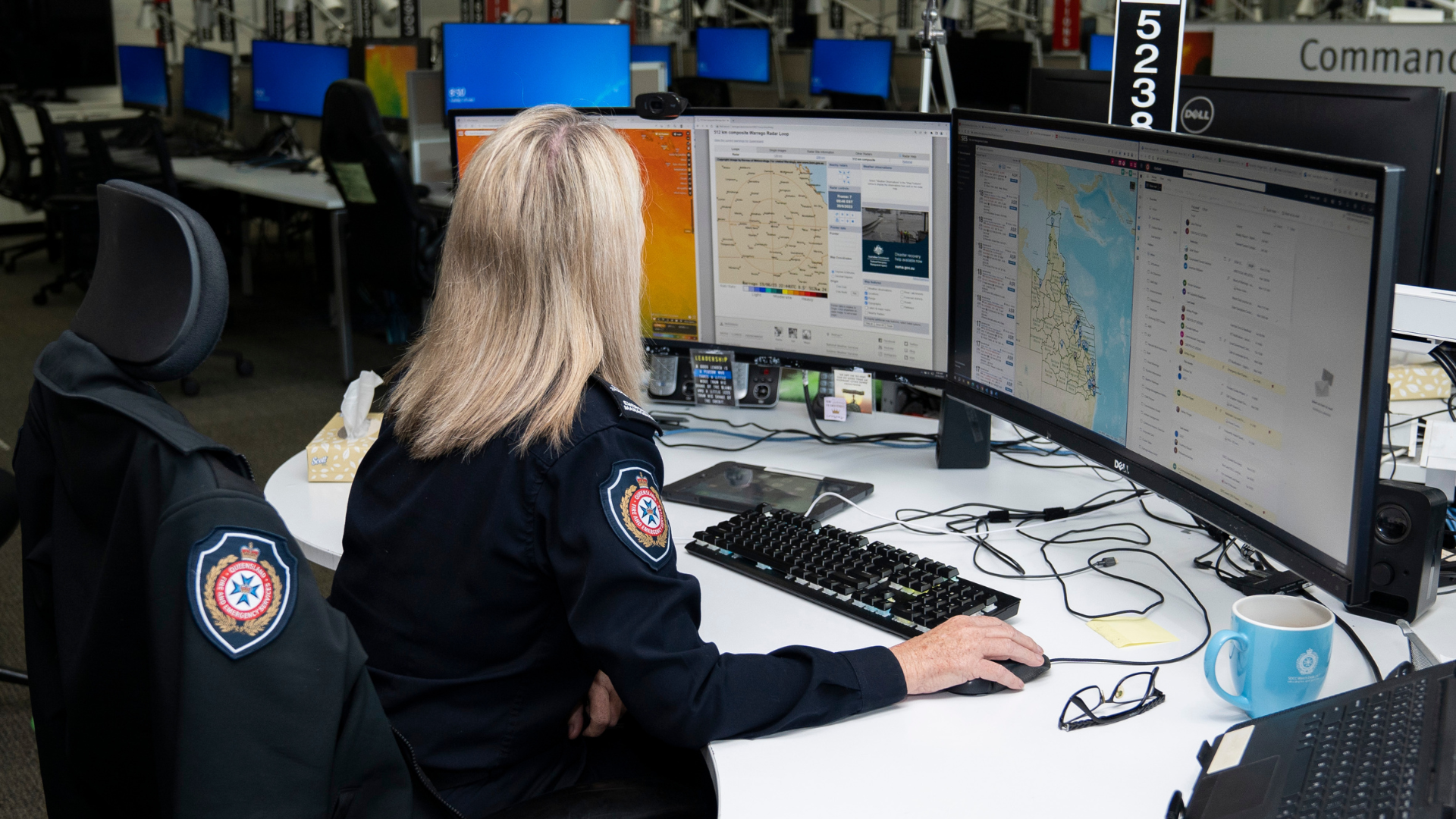 A person sitting at a desk with multiple computer screens in the QFES watchdesk.