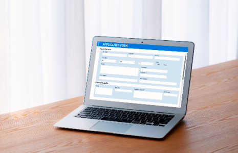 A laptop on a table. The screen is displaying an application form.