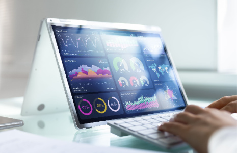 A 2-in-1 laptop screen displays a statistical dashboard. Some hands are on a keyboard in front of the laptop.